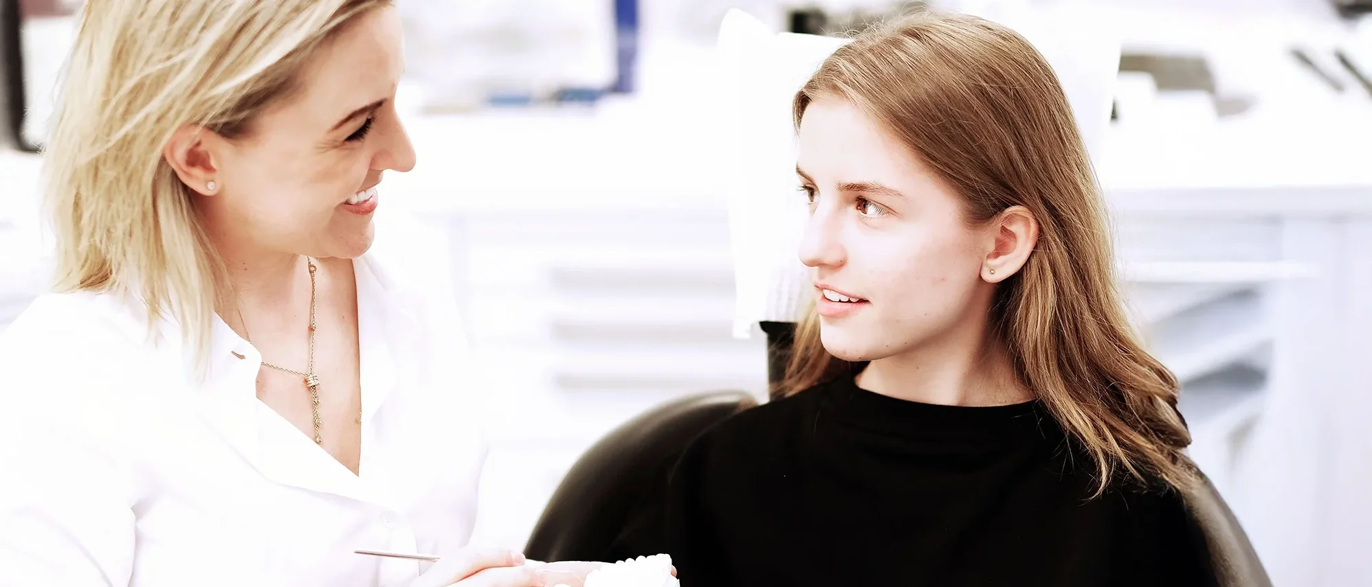 Zahnärztin erklärt einer jungen Patientin eine Behandlung anhand eines Zahnmodells
