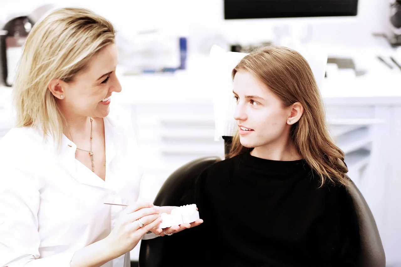 Dentist explains treatment to a young patient using a dental model