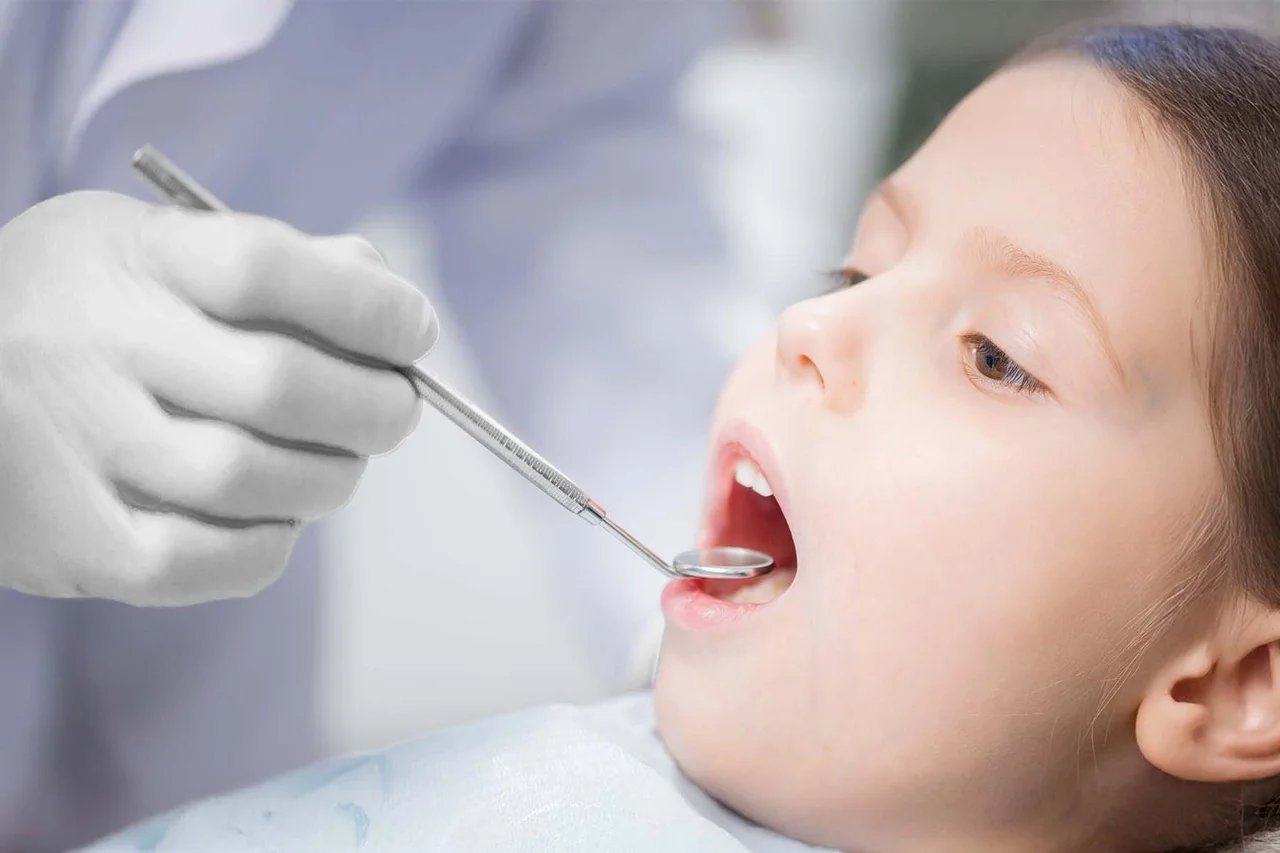 Child is examined by a dentist using a dental mirror