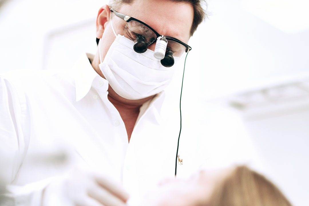 Herr Dr. Krieter hat eine Lupenbrille auf während er neben einer Patientin in der Zahnarztpraxis in Regensburg steht